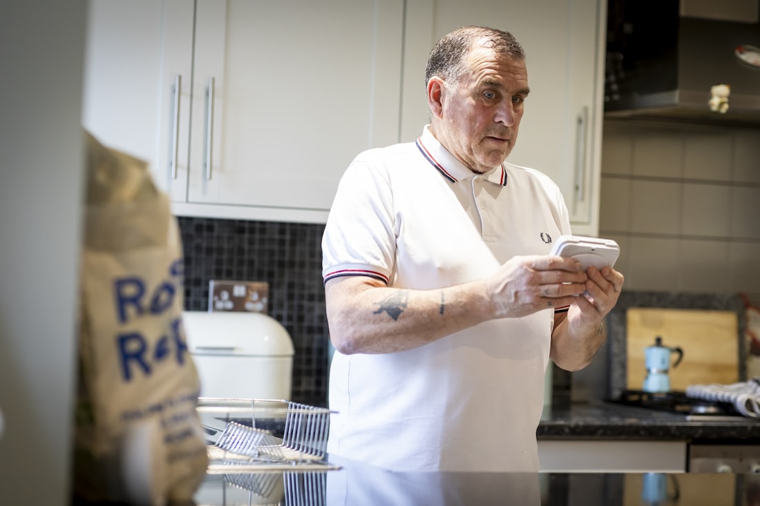 Man regelt zijn energiecontract op zijn telefoon in de keuken